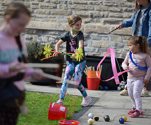 Two young children with circus equipment, one with a twirling ribbon and one with a balancing set