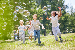 A group of children running in a field chasing after big bubbles.