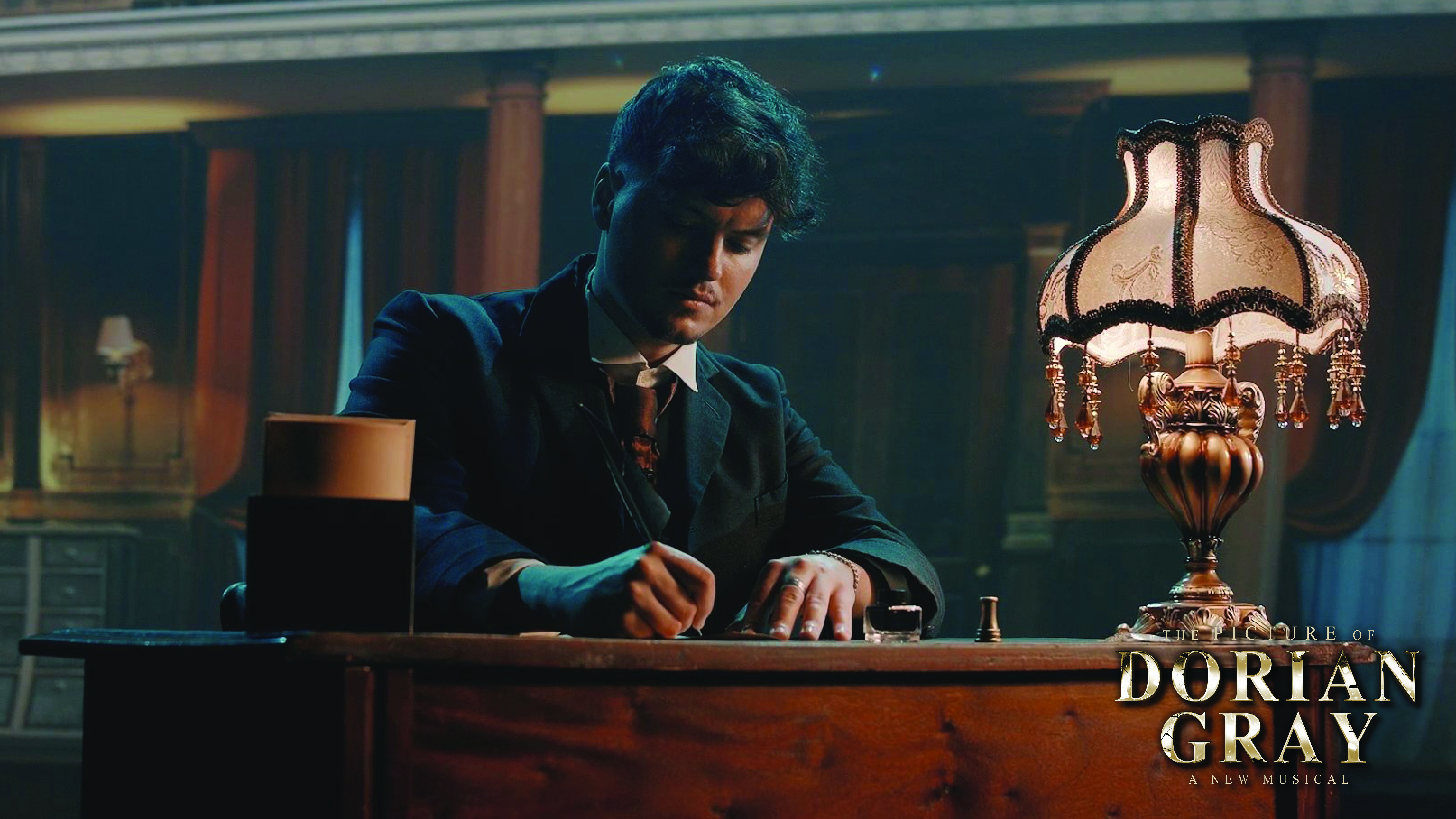 Promotional image for The Picture of Dorian Gray: A New Musical, featuring a performer writing at a desk beside an antique lamp in a Victorian-inspired setting.