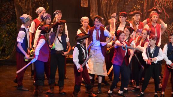 Children in pirate costumes performing a stage scene with toy swords during a theatre production.