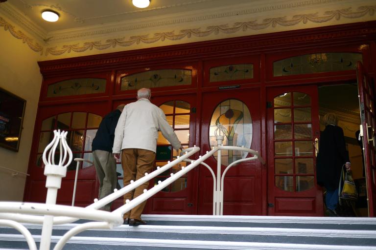 Visitors enter a historic building through red stained-glass doors via a stepped entrance.