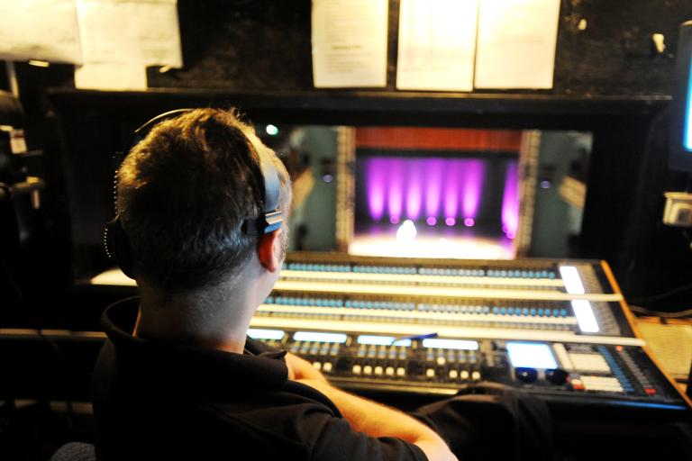 Technician at a lighting desk overlooking the Palace Theatre stage during a performance setup.