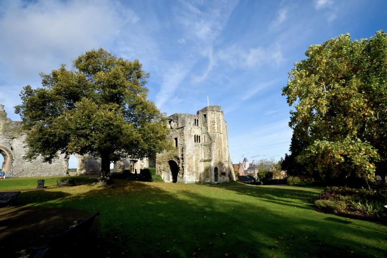 Newark Castle ruins surrounded by green lawns and mature trees under a bright blue sky.