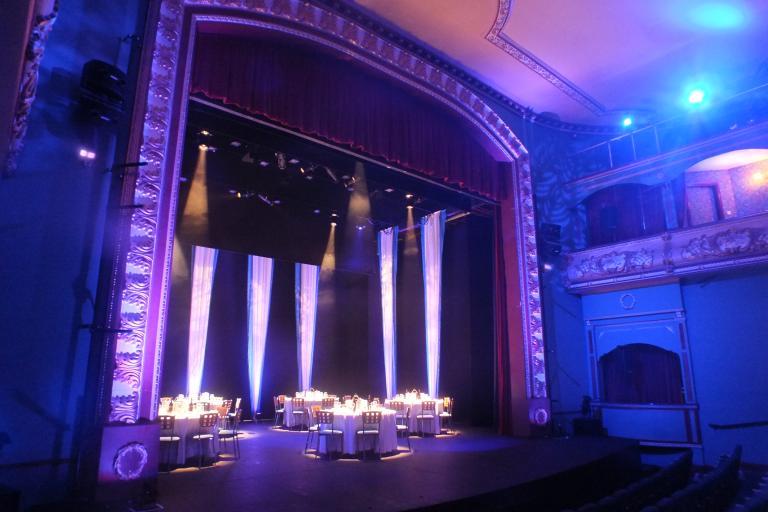 Banquet tables set on the Palace Theatre stage beneath dramatic lighting and red curtains.
