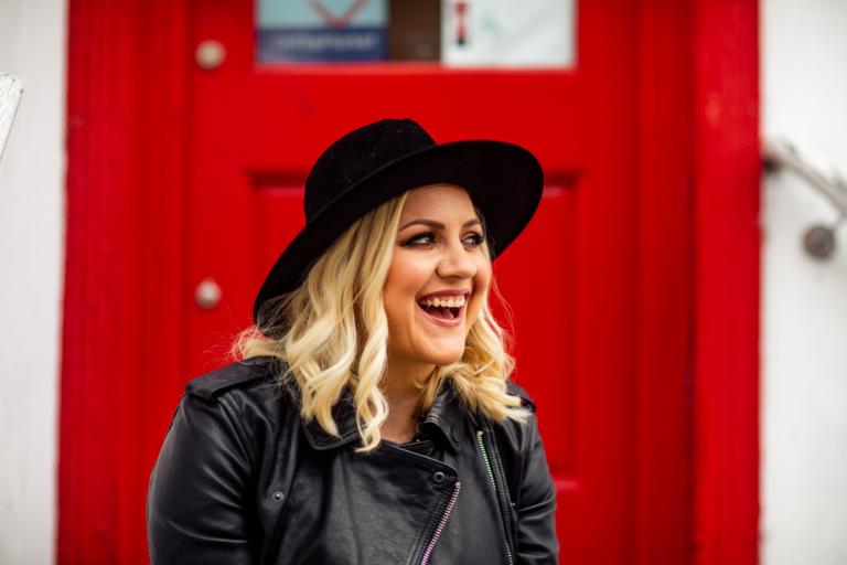 Acclaimed singer-songwriter Phillipa Hanna sat smiling in front of a red door.