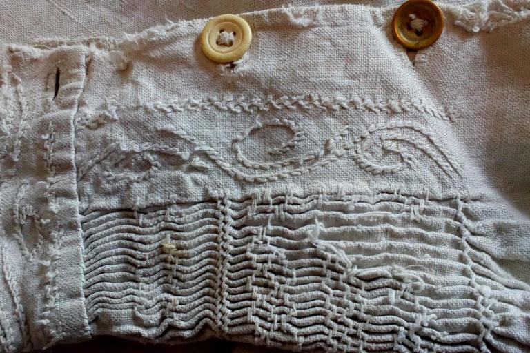 Close-up of a historic smocked linen garment featuring decorative hand stitching, buttons and traditional textile craftsmanship.
